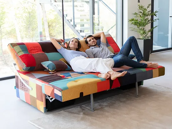Canapé relax convertible Fama Indy avec deux personnes, présenté dans un intérieur lumineux – Meubles Bouchiquet à Bergues (59)
